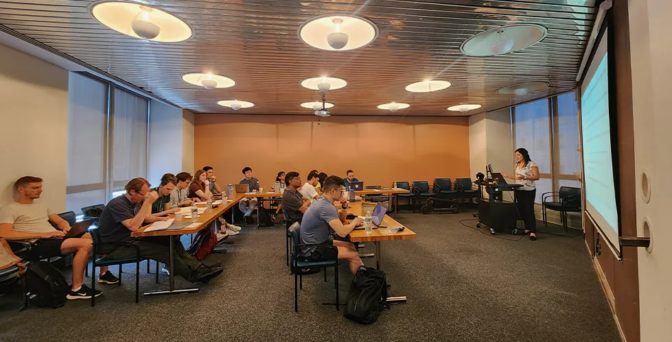 a group of people sitting at desks and listening to a presenter in a classroom