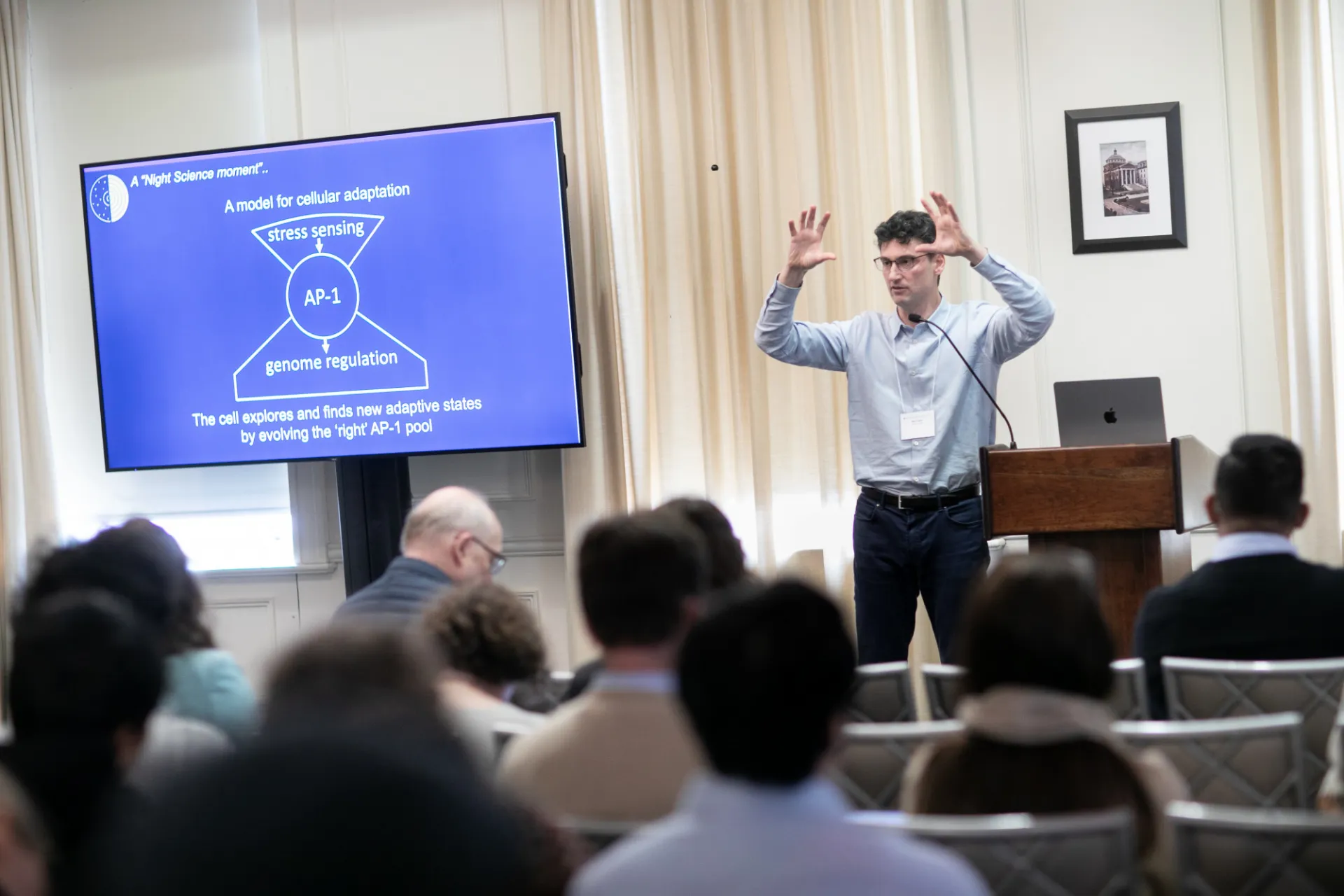 Itai Yanai stands in front of a crowded room at a podium and presents a PowerPoint.