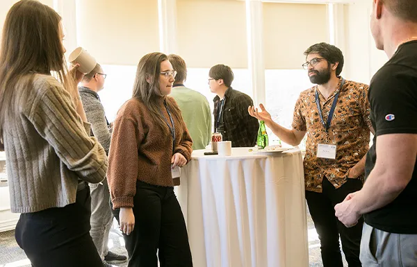 Graduate students stand around a high-top table having a discussion at an event