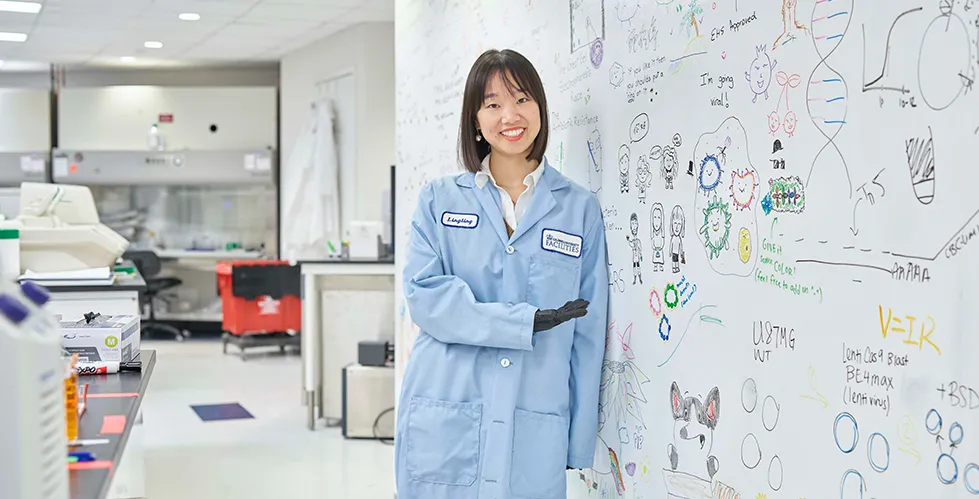 Lingting Shi, PhD wears a labcoat and stands by a whiteboard in the McFaline-Figueroa Lab.
