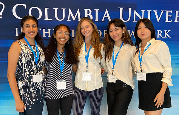 Group of five students standing in front of Columbia University banner
