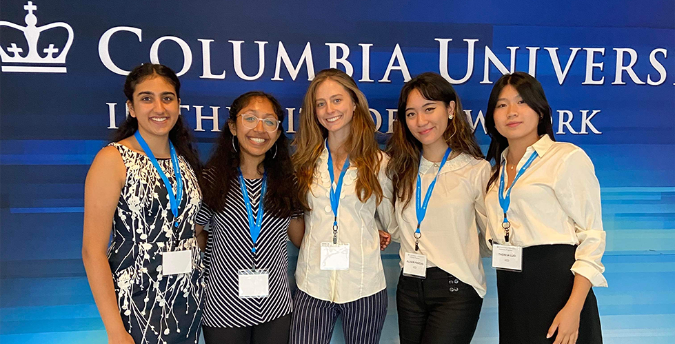 five women standing in front of a blue wall with the Columbia university logo