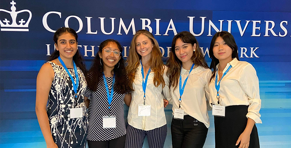 IICD SRP interns. From left to right: Isha Arora, Sruthi Parthasarathi, Mackenzie Schiller, Allison Pascual, Theresa Luo five women standing in front of a blue wall with the Columbia university logo