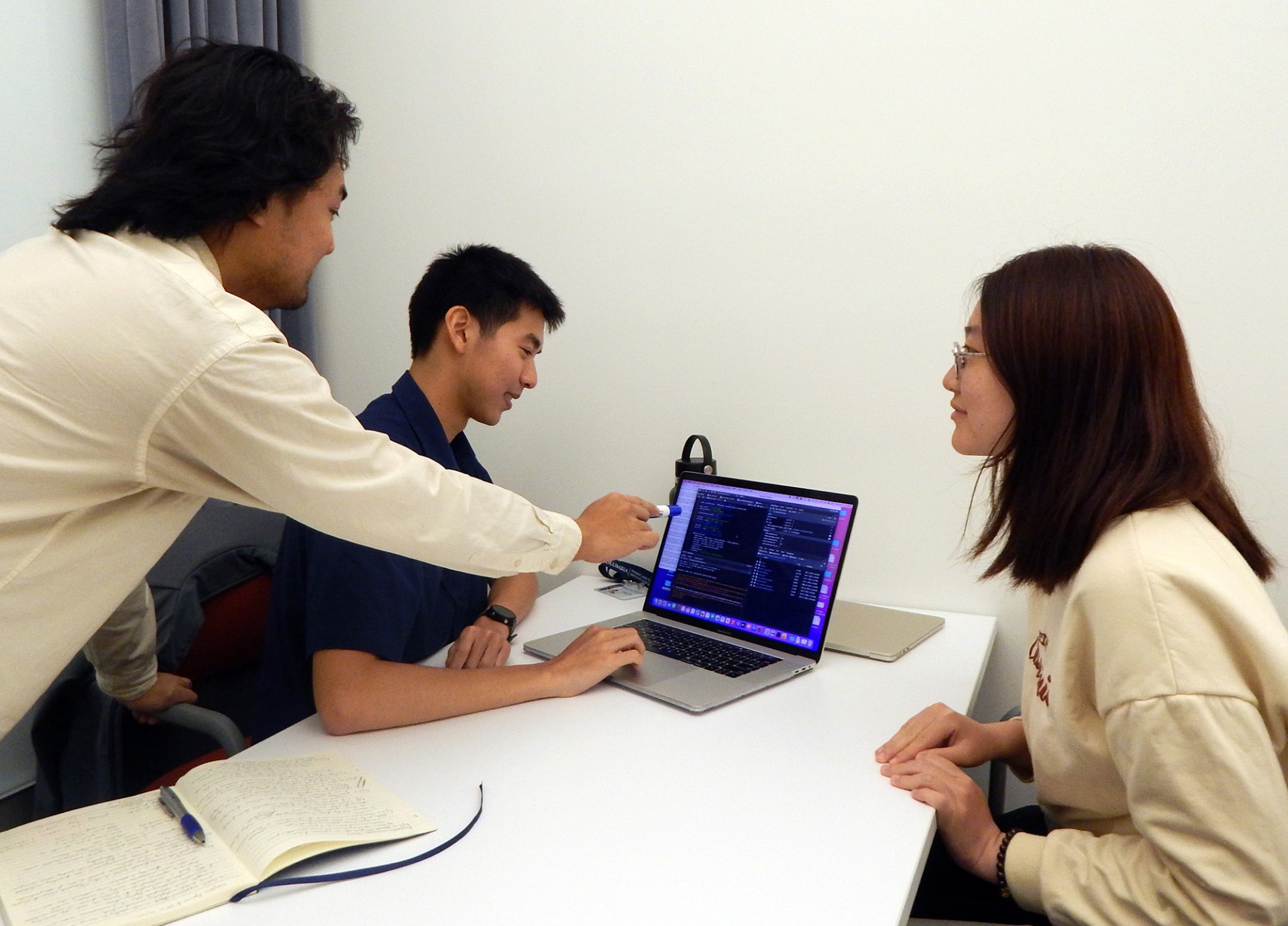 a group of three people discussing around a desk, looking at a laptop. 