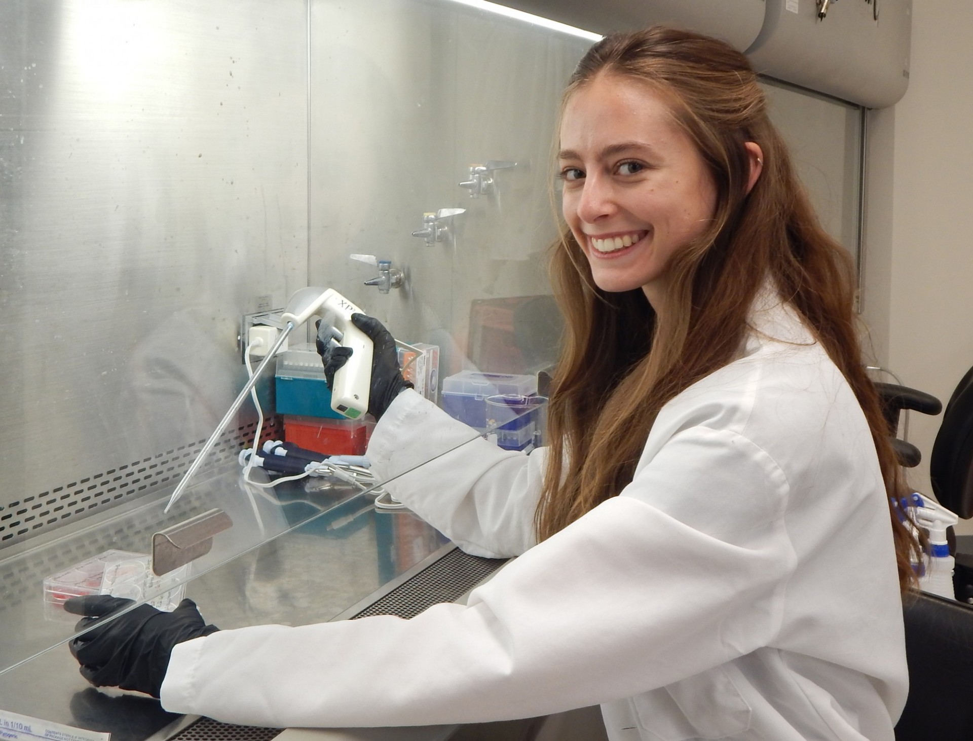 A woman student seating and pipetting under the hood